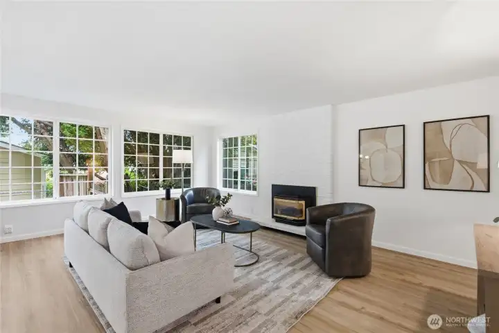 Alternate angle highlights the generous layout, corner window bank, and brick fireplace — a light-filled space designed for relaxed gatherings.