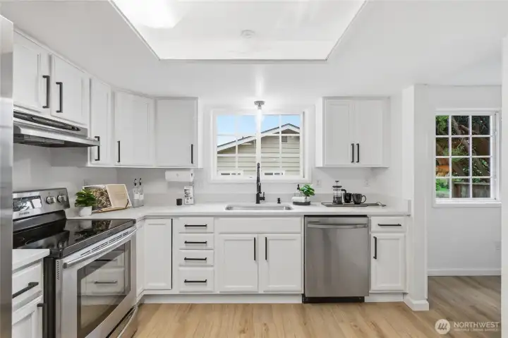 Fully updated kitchen with white shaker cabinetry, black hardware, quartz countertops, stainless steel appliances, and a skylight detail overhead.