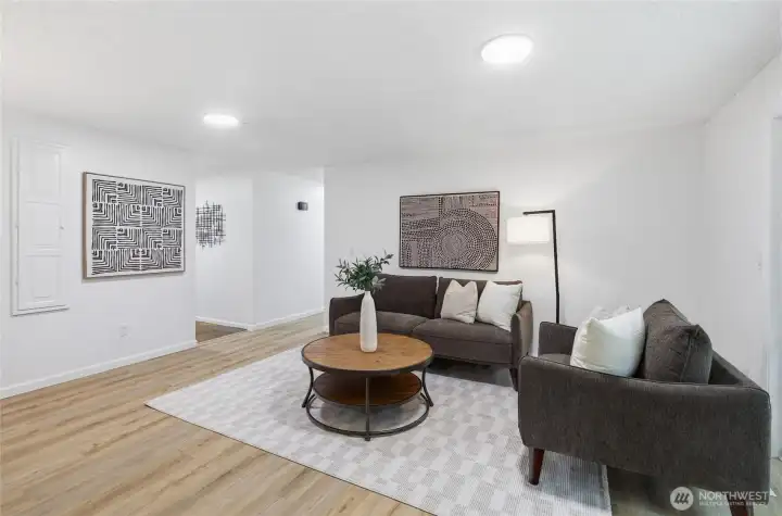 Alternate angle of the family room highlights the open layout, wood-look floors, and easy flow toward the entry and kitchen.