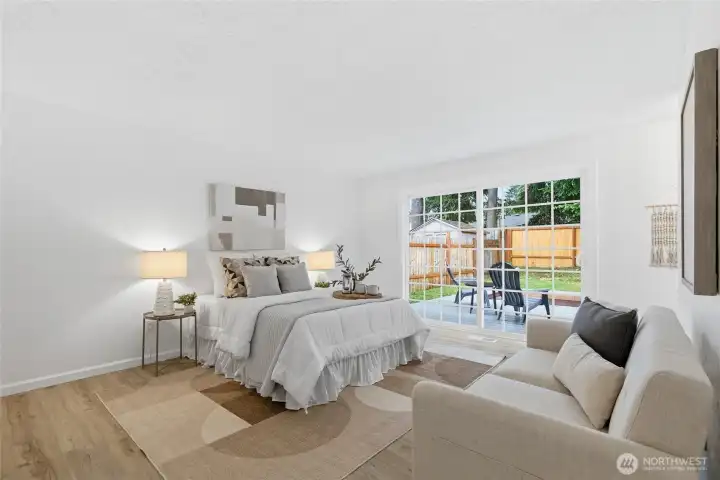 Spacious primary suite with sliding glass door to the back patio, wood-look floors, and room for a dedicated sitting area.