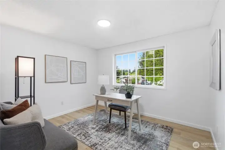 Sunlit secondary bedroom with a large grid window, wood-look floors, and enough space to serve as a home office or guest room.