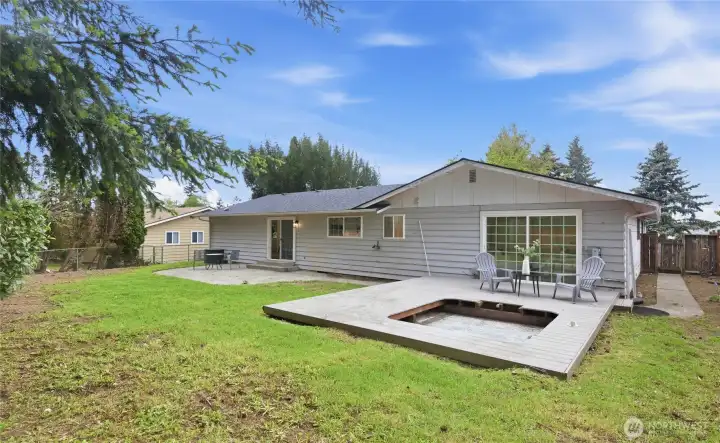 Wide backyard view highlighting the low-profile deck with in-ground feature, generous lawn space, and fully fenced perimeter backed by mature evergreens.