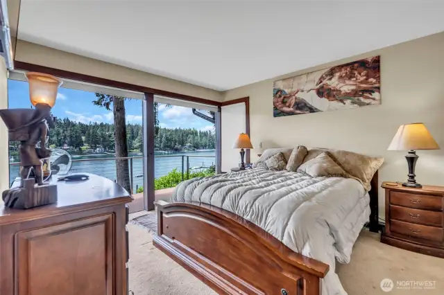 Primary bedroom with ensuite on the main floor. Sunset and water views. Built-in wall mount TV. Wall of windows plus corner window looking towards the entry of Manzanita Bay. Closet plus a hallway with built in dresser and cabinets above.