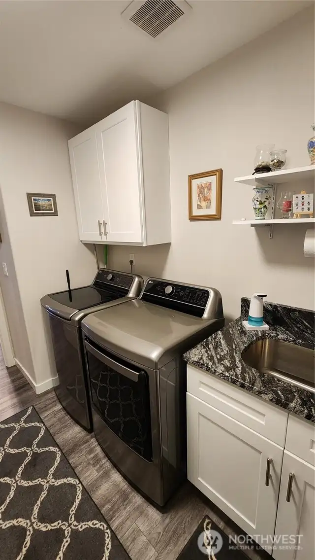 Utility room has a utility sink and added cabinets and shelving besides large washer and dryer.