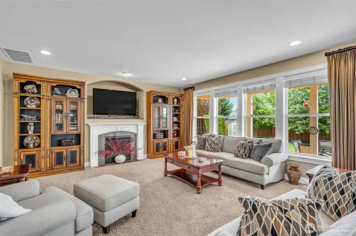Inviting family room featuring a cozy gas fireplace, custom built-in cabinetry, and expansive windows that fill the space with natural light while showcasing views of the private backyard. Inviting family room featuring a cozy gas fireplace, custom built-in cabinetry, and expansive windows that fill the space with natural light while showcasing views of the private backyard.