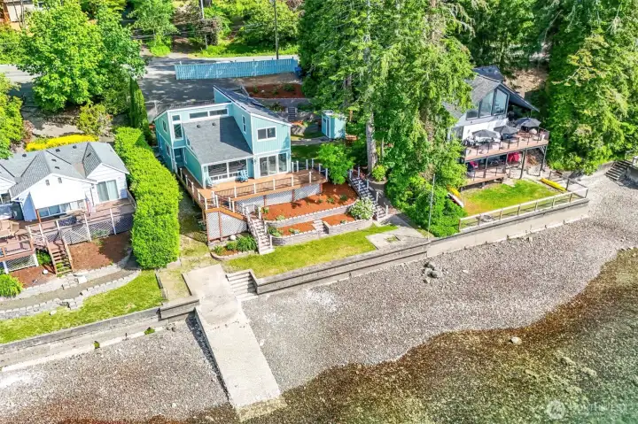 From the water looking back, the home is nothing short of striking. The freshly painted sage green exterior rises confidently above the terraced, meticulously landscaped yard — layers of stone retaining walls, manicured lawn, and lush plantings cascading down toward the beach. The sweeping deck wraps the back of the home, perfectly positioned to capture every angle of the water and the mountain views beyond.  On clear days, the Olympic Mountains paint the horizon in a way that never gets old — whether you're sipping morning coffee, grilling at sunset, or simply sitting in the quiet and letting the view wash over you.  Low tide reveals the full magic of Hood Canal — the rocky shoreline, the clarity of the water, the sheer sense of space that only true waterfront living delivers and sitting above the tide lines offers complete peace of mind.