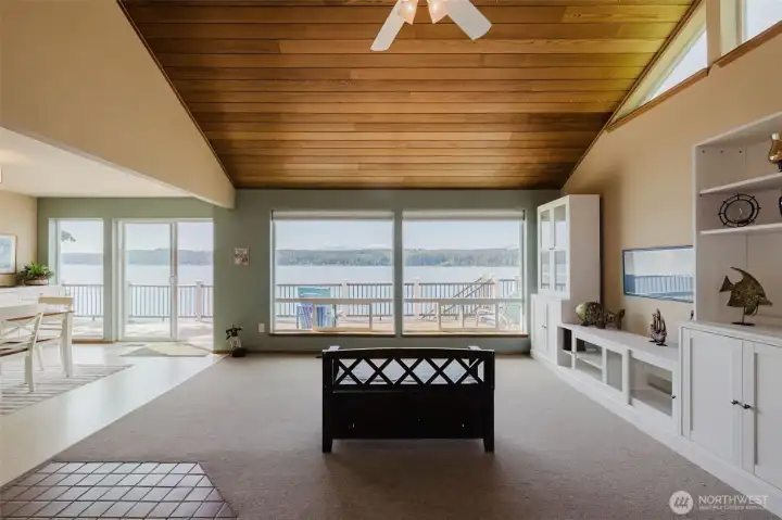 Step inside and stop. Just stop. Floor-to-ceiling new windows frame an unobstructed panorama of Hood Canal that stretches as far as the eye can see — shimmering water, forested hillsides, and mountain peaks beyond. This is not a room with a view. This is a view with a room built around it.  Overhead, rich warm wood ceilings wrap the space in the kind of natural beauty that no paint color or finish can replicate. The grain, the warmth, the way the light plays across it at different times of day — it gives this living room a soul that you feel the moment you walk in.  The brand new windows do more than frame that spectacular waterfront panorama — they flood the space with natural light from morning to evening, making every hour of the day feel like golden hour. Whether the tide is in or out, whether the canal is glassy calm or dancing with afternoon chop, the view from this living room is endlessly captivating.