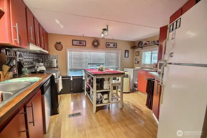 Spacious kitchen view with island prep space, dining area, and window light. Spacious kitchen view with island prep space, dining area, and window light.