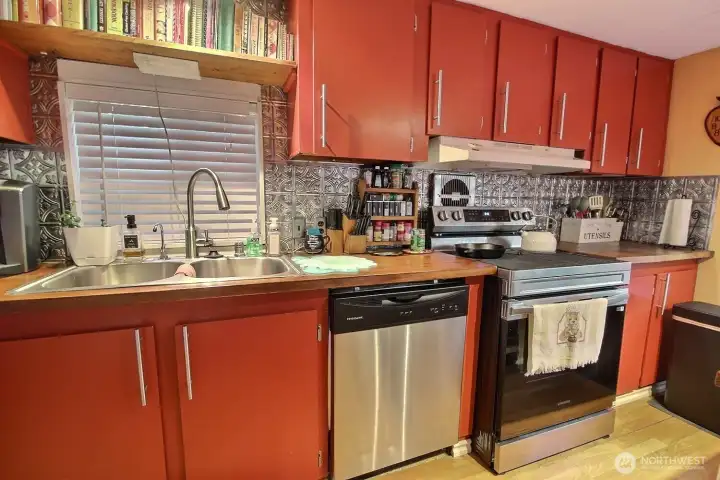 Kitchen with red cabinetry, dishwasher, range, sink, and tile-style backsplash. Kitchen with red cabinetry, dishwasher, range, sink, and tile-style backsplash.