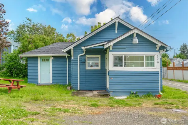 This welcoming exterior showcases the home’s freshly painted facade, crisp white trim, and covered entry leading into the laundry/mudroom. The additional door to the left offers access directly into the living room. Large windows brighten both spaces, while the open yard adds potential for outdoor enjoyment or future personalization.