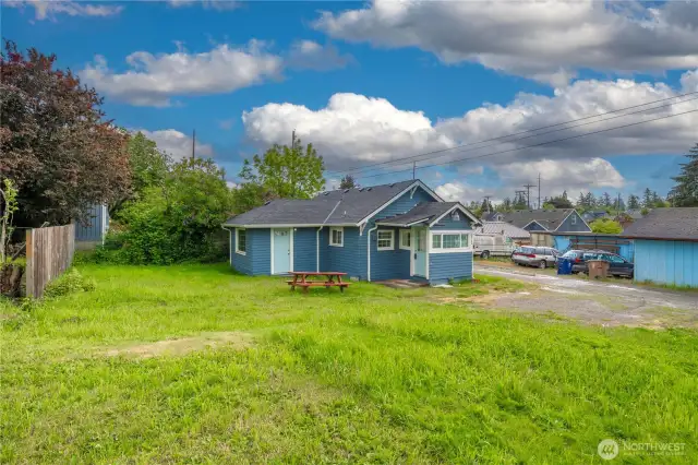 This wider perspective shows off the generous yard space—perfect for gardening, play, or future projects. The home sits with alley access and features two entry points: a side door leading into the living area and a front entry through the mudroom/laundry area. The vibrant blue exterior adds charm, while the picnic table invites you to enjoy outdoor moments in your own slice of Tacoma.