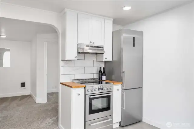 This well-appointed kitchen makes the most of its footprint with a modern stainless steel range, sleek vent hood, and matching fridge—all set against a backdrop of crisp white cabinetry and striking tilework. A touch of butcher block warmth frames the cooking space, blending efficiency and style in perfect balance. Ideal for any home chef or weekend cook who values both form and function.