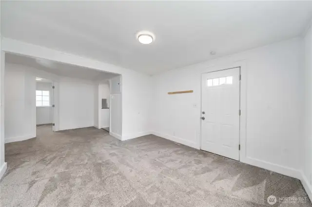 From this angle, you can see how the living area flows naturally into the kitchen and bedroom, making the most of its compact layout. Fresh carpeting and neutral tones make this space move-in ready and easy to personalize. The front entry adds convenience and charm.