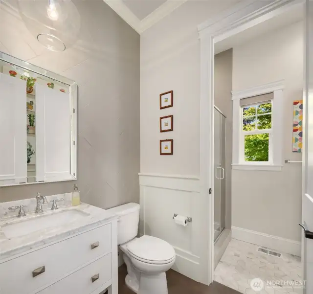 Thoughtfully designed main floor bath featuring a marble-topped vanity, stylish tilework, and a light-filled walk-in shower. Dual access from both the main living area and the adjacent bedroom allows for flexible use—easily functions as a powder room day-to-day, or opens up as a full guest bath when needed.