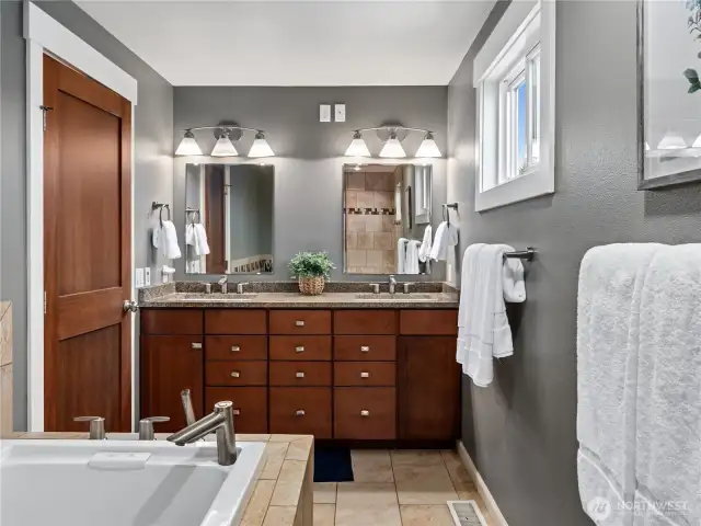 The spacious and modern primary bathroom, featuring a grand double vanity with tasteful wood cabinetry and beautiful granite countertops.