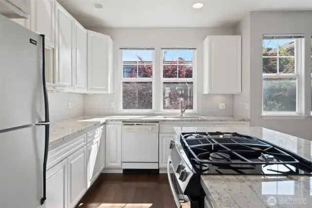 Bright white kitchen with gas range and updated granite counters and tile backsplash