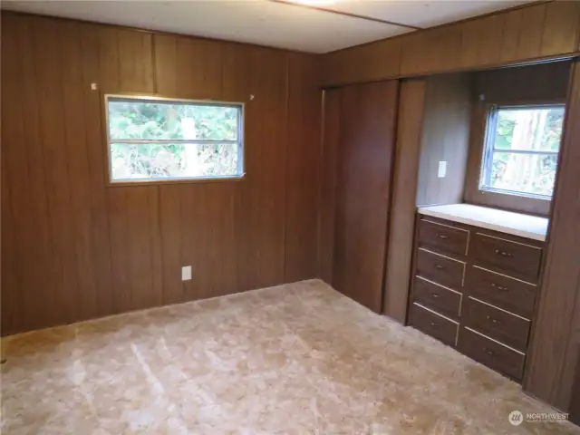 Larger bedroom in back of the home. Wooded areas behind the home and seen from these windows.  To the right are two closets on either side of the counter under the windows with drawers below.