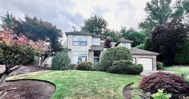 Full front view of home from sidewalk looking up to sloped driveway and additional plantings and landscape