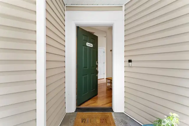 A charming covered entry welcomes you with a classic green door, warm wood floors, and a bright, inviting interior just beyond.