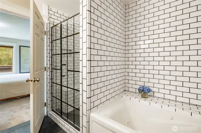 Beautiful primary bathroom tub and shower finished in white subway tiles with black accents.