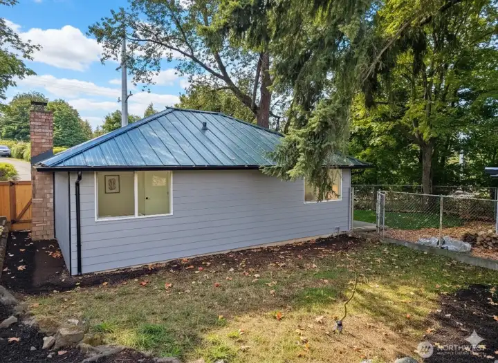 Rear side of the home with two bedroom windows overlooking a private, fenced backyard — complete with a gated dog run or garden area. Quiet, shaded, and easy to maintain.