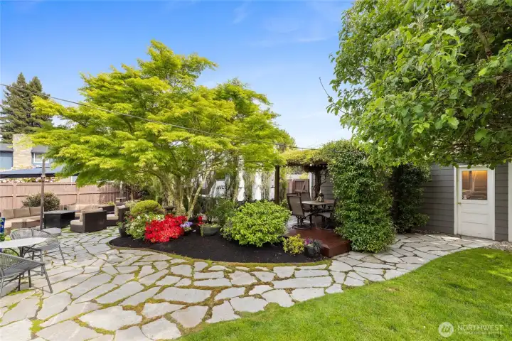Park-like backyard oasis featuring mature landscaping, expansive stone patios, covered pergola dining area, and multiple spaces designed for relaxing and entertaining.