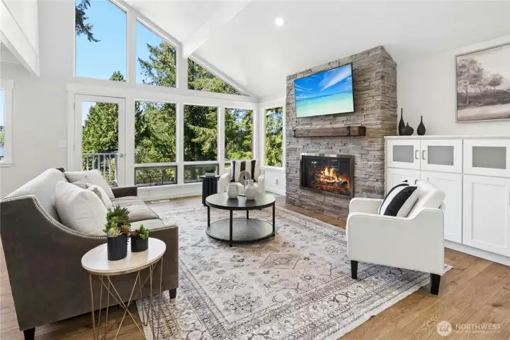 A wall of window invites sunlight and views into this light and airyl living room. A stylish stone fireplace is flanked by media cabinets.