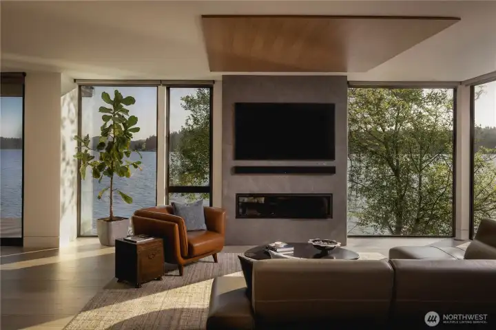 The living room is anchored by a fireplace wall, with surrounding glass framing the lake and bringing balance to the space.