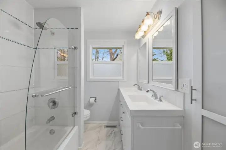 Bathroom with double sinks, tile shower/tub combo and window for natural light.
