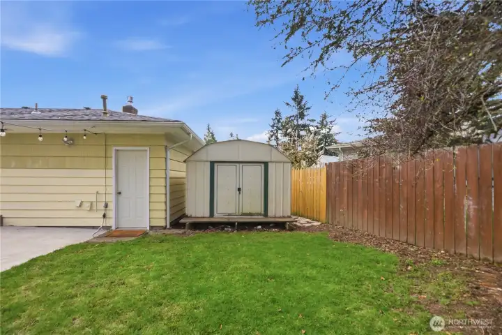 Storage shed with convenient garage access in fenced backyard.
