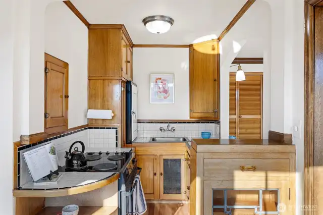 The kitchen is a charming blend of vintage character and function, featuring a built-in hutch with an original leaded-glass window, classic tile countertops and backsplash, and beautifully preserved glowing wood cabinetry. Thoughtful details like an old-fashioned icebox add to its timeless appeal.