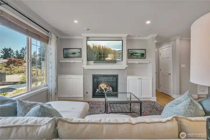 Living room features a gas fireplace with custom built-ins and large picture window bringing in natural light.