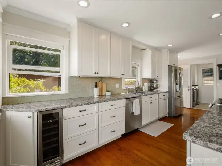 White shaker style cabinets and natural stone counter tops adorns the functional kitchen. Stainless steel appliances include a wine fridge.