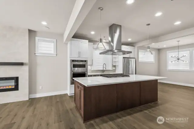 The kitchen is at the heart of the home featuring a large island with seating, pendant lights, a 5-burner gas cooktop with extraction hood, and thick slab quartz countertops.  The family room and dining room are flanked on both sides of the kitchen.