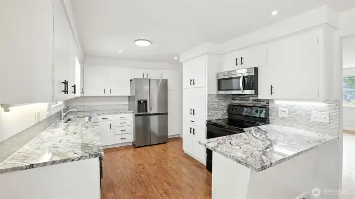 Updated kitchen that features newer grab handles, tile backsplash, light fixtures, laminate flooring, and appliances.