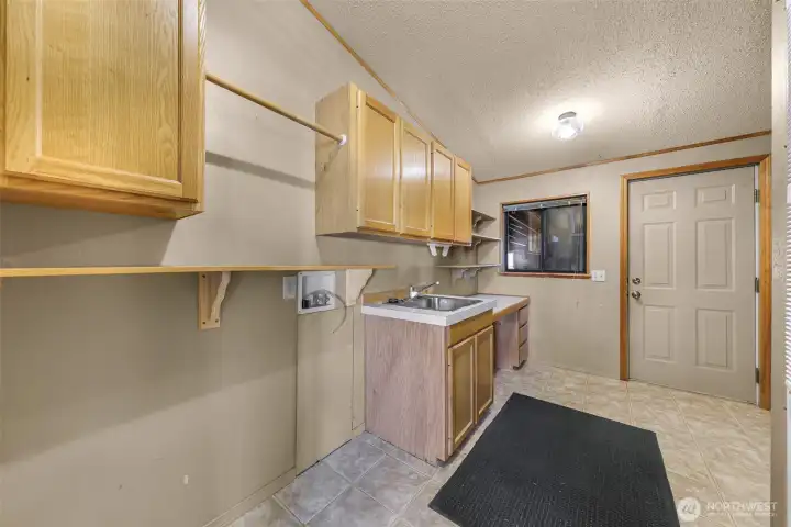 Full utility room with sink and folding counter and additional storage space, leads to enclosed garage and workshop