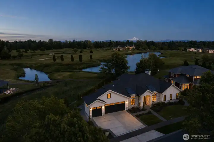 Twilight aerial capturing the home's exceptional position along Loomis Trail Golf Course with mountain views beyond.
