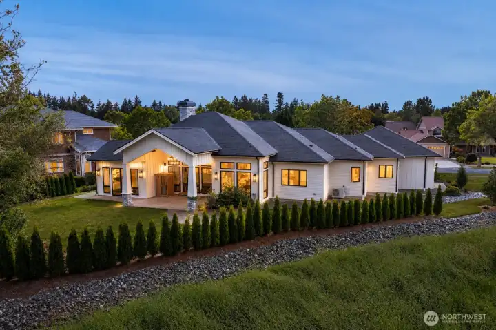 Twilight aerial capturing the home's rear elevation, outdoor entertaining areas, and exceptional position within The Greens at Loomis Trail, space for hot tub, on pad.