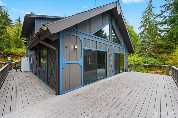Surrounded by lush evergreens, this distinctive chalet-style home showcases vaulted windows and expansive wraparound decking designed for seamless indoor-outdoor living.