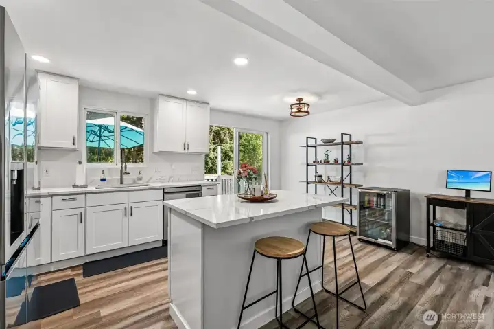 Remodeled kitchen with Quartz counters, island, stainless steel appliances and a sliding glass door to deck overlooking back yard