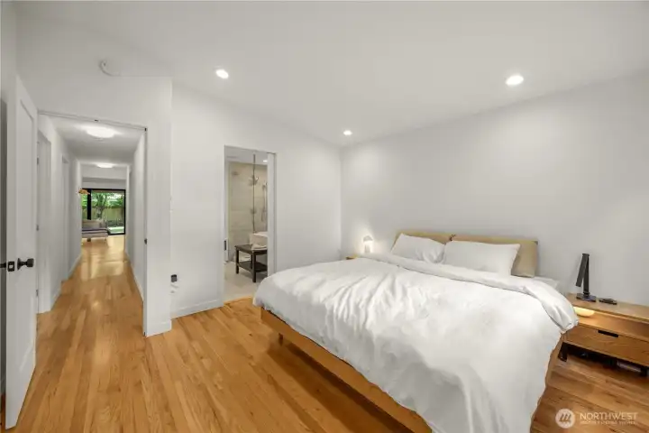 Light-filled primary suite featuring an en suite bath, walk-in closet with custom built-in shelving, and refinished hardwood floors.