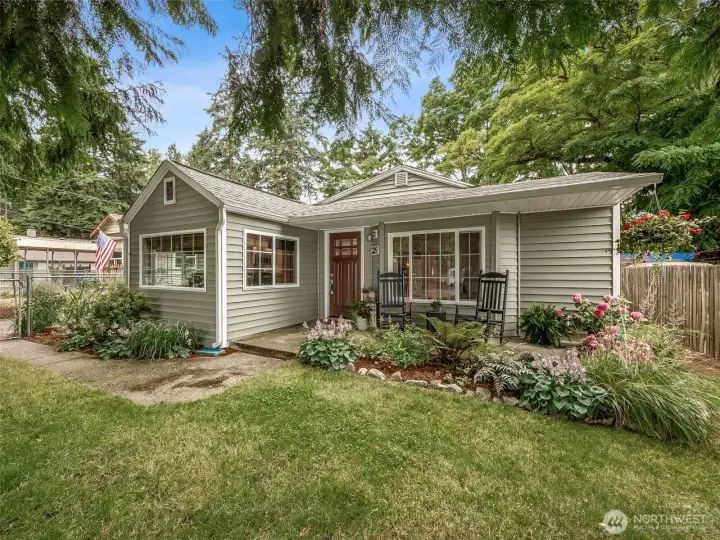 Charming curb appeal with cottage-style landscaping! The inviting rambler features a welcoming covered front porch, lush perennial gardens, mature landscaping, large picture windows, and timeless Northwest charm.