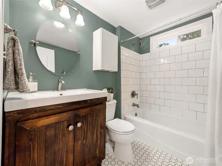Thoughtfully renovated bathroom blends timeless style with modern convenience, offering a subway tile shower/tub surround, contemporary vanity, hex tile flooring, and updated lighting and fixtures