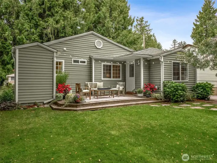 Private backyard oasis featuring a spacious entertainment deck, lush level lawn, colorful landscaping, and mature evergreens—an ideal setting for relaxing or hosting guests