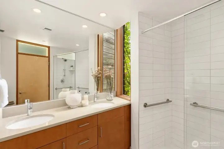 The dual vanity’s natural wood cabinetry and quartz counters are enhanced by the optional illusion of a creatively-placed window – allowing natural light into the room while preserving privacy and creating a surprising reflection that may take a minute to absorb – a very cool touch this unit enjoys thanks to being a corner unit with gorgeous greenery out the window.