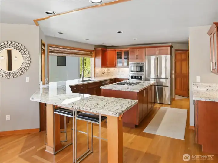 Stunning kitchen features a spacious island cooktop, gleaming stone counters throughout, and a raised breakfast bar perfect for casual dining