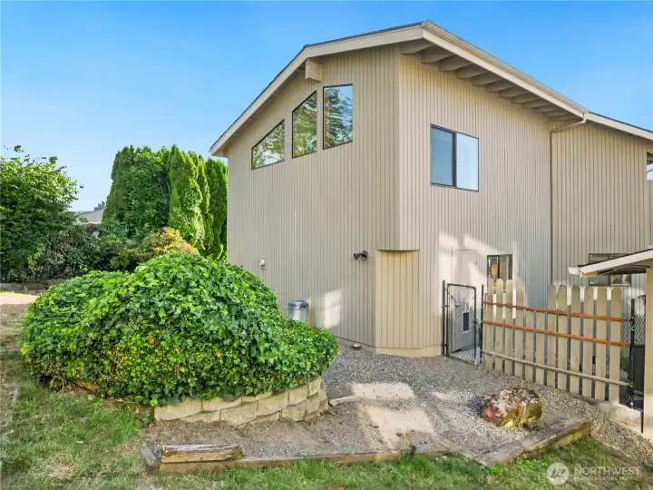 Tucked-away side yard with gated access, mature plantings, and a low-maintenance gravel area