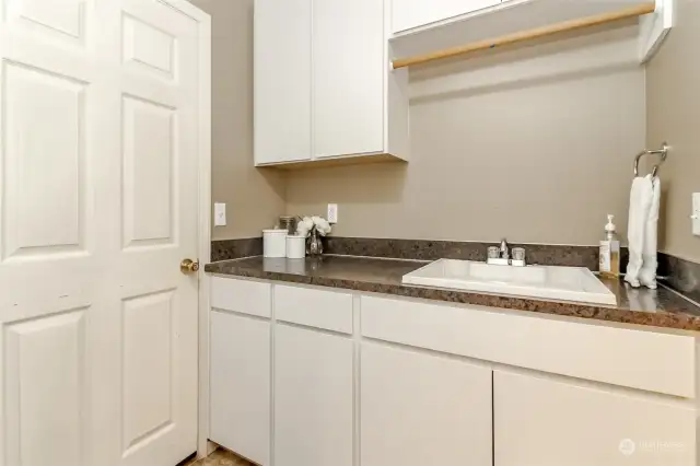 More cabinets in utility room with large utility sink, drying pole and garage door to the left.