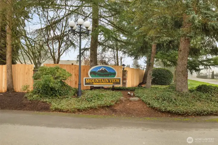 Welcoming entrance to this well-maintained community, framed by mature trees and lush landscaping, creating a warm first impression as you arrive home.