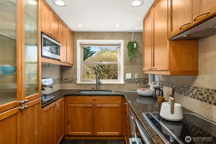 The kitchen features updated stainless steel appliances, a new kitchen hood vent, wood cabinetry and slate flooring.